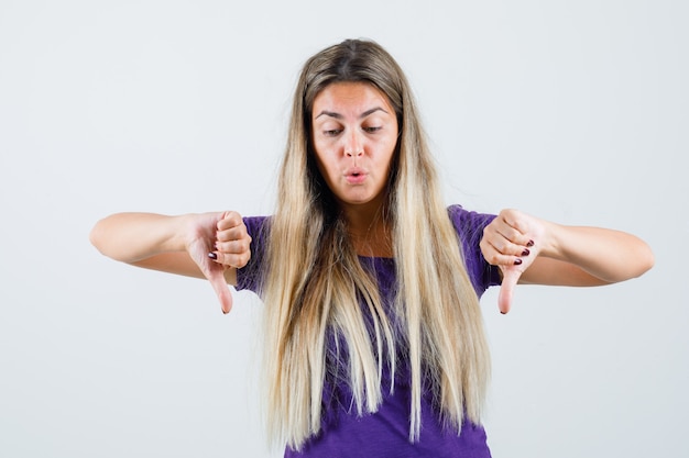 Free photo blonde lady showing double thumbs down in violet t-shirt and looking focused , front view.