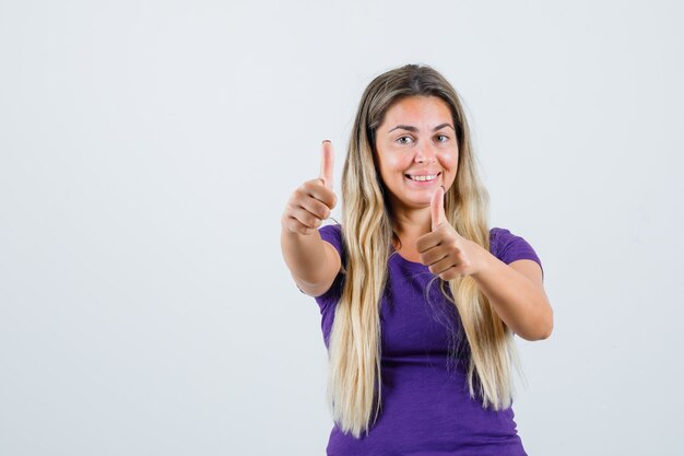 Blonde lady showing double thumbs up in violet t-shirt and looking glad , front view.