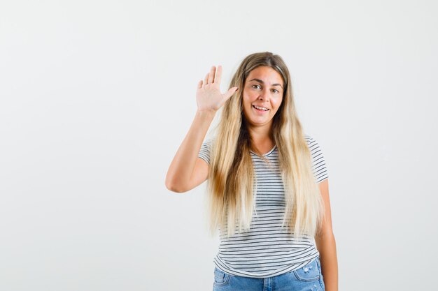 Blonde lady showing greeting gesture in t-shirt and looking merry , front view.