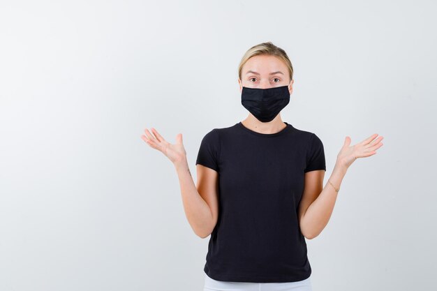 Blonde lady showing helpless gesture in black t-shirt isolated
