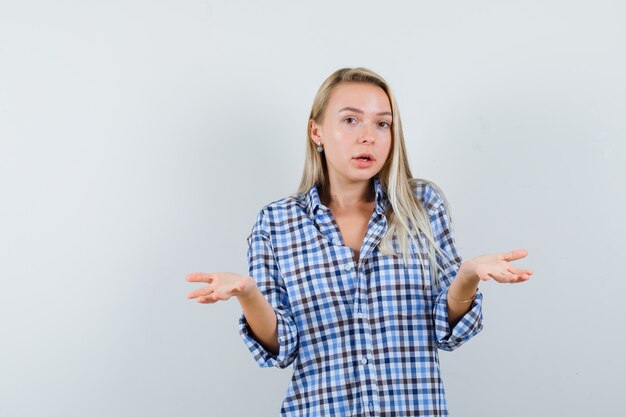 Blonde lady showing helpless gesture in casual shirt and looking confused