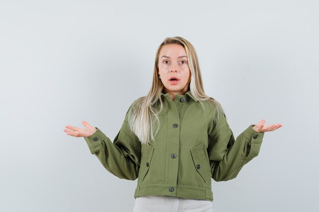 Blonde lady showing helpless gesture in jacket, pants and looking perplexed , front view.