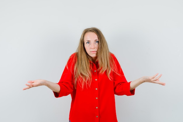 Blonde lady showing helpless gesture in red shirt and looking confused.