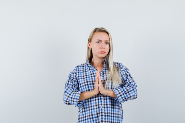 Free photo blonde lady showing namaste gesture in checked shirt and looking doubtful