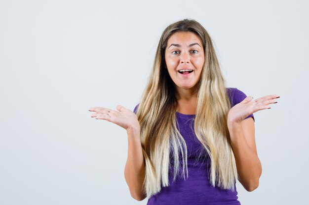 Blonde lady showing open palms in violet t-shirt and looking happy. front view.