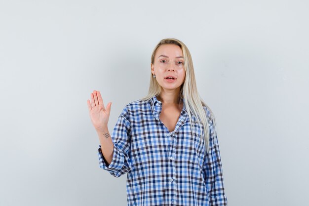 Blonde lady showing palm in checked shirt and looking confident