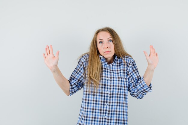 Blonde lady showing palms in surrender gesture in shirt and looking scared ,