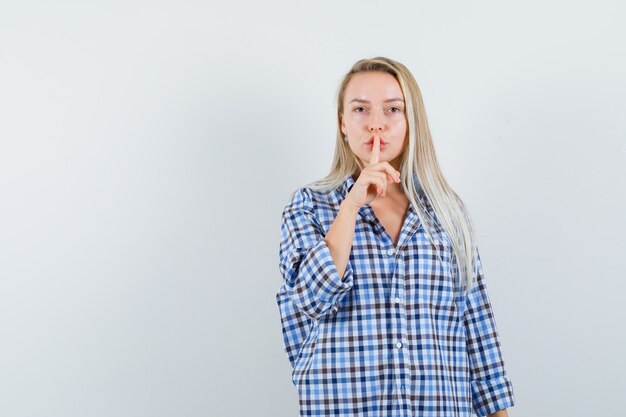 Blonde lady showing silence gesture in checked shirt and looking sensible