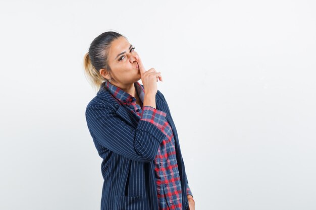 Blonde lady showing silence gesture in shirt, jacket and looking confident. front view.