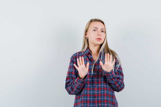 Blonde lady showing stop gesture in casual shirt and looking serious. front view.