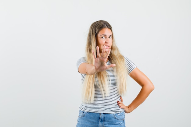 Blonde lady showing stop gesture in t-shirt and looking serious. front view.