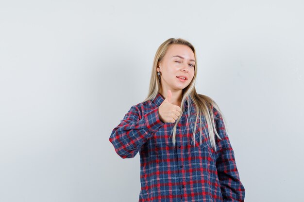 Blonde lady showing thumb up in casual shirt and looking confident. front view.