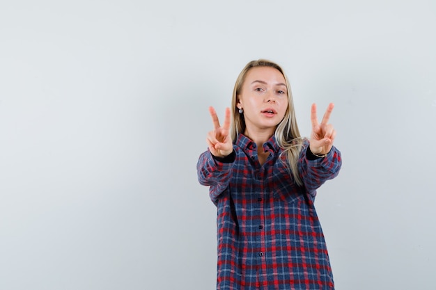 Blonde lady showing V-sign in casual shirt and looking confident , front view.