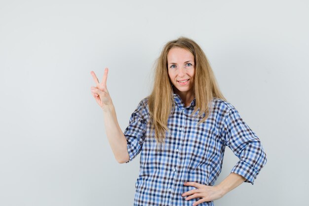 Blonde lady showing victory gesture in shirt and looking cheerful ,