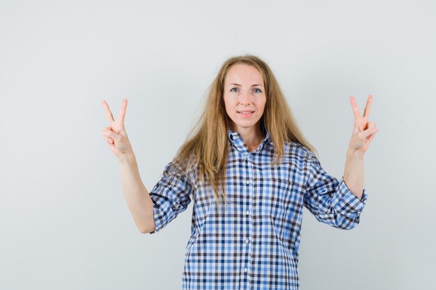 Blonde lady showing victory gesture in shirt and looking confident.