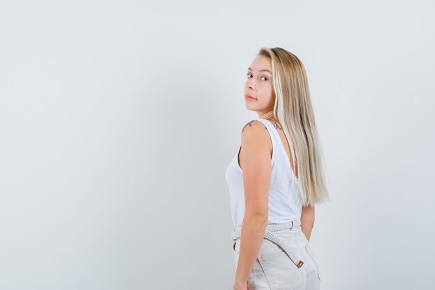 Blonde lady in singlet, pants looking over her shoulder and looking elegant .