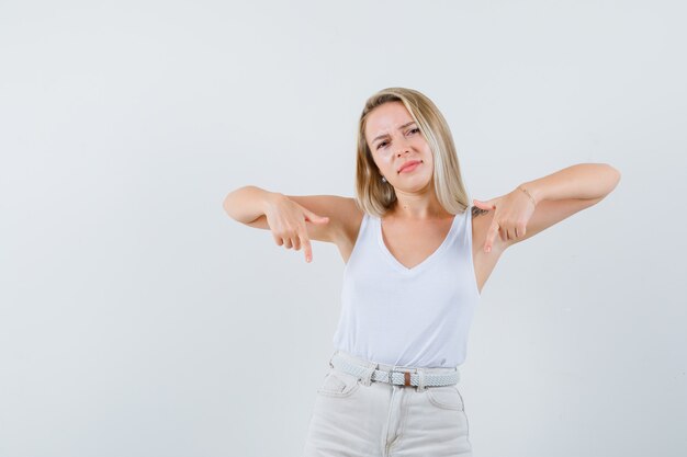 Blonde lady in singlet, pants pointing down and looking confident