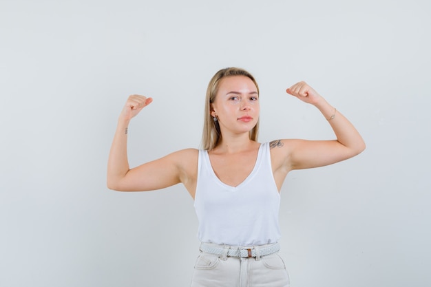 Foto gratuita signora bionda in canottiera, pantaloni che mostrano i muscoli delle braccia e che sembra sicura di sé, vista frontale.