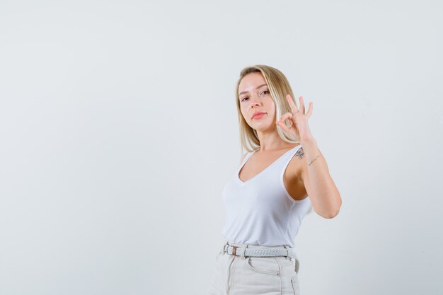 Blonde lady in singlet, pants showing ok gesture and looking confident