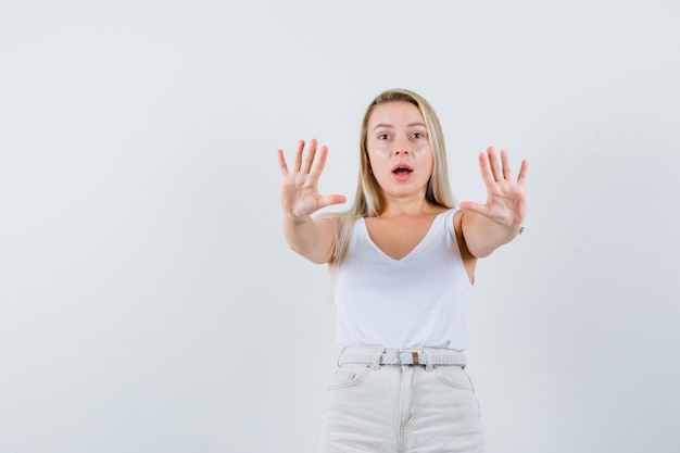 Blonde lady in singlet, pants showing refusal gesture and looking anxious