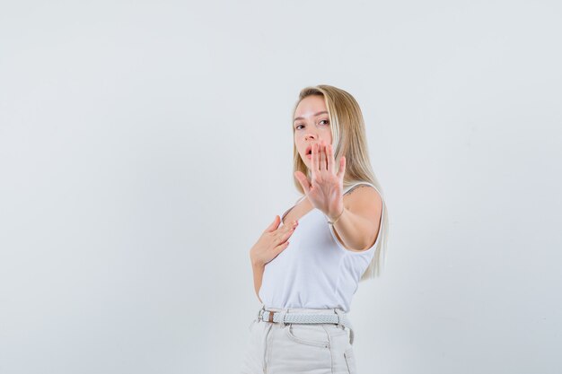 Blonde lady in singlet, pants showing stop gesture and looking alarmed