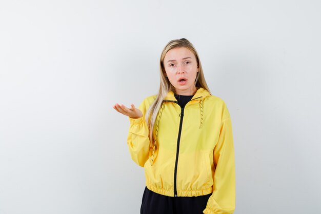 Blonde lady spreading palm aside in tracksuit and looking puzzled , front view.