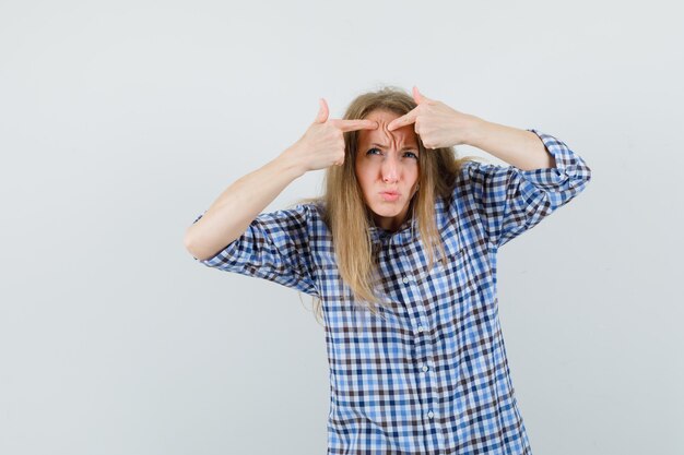 Blonde lady squeezing her pimple on forehead in shirt