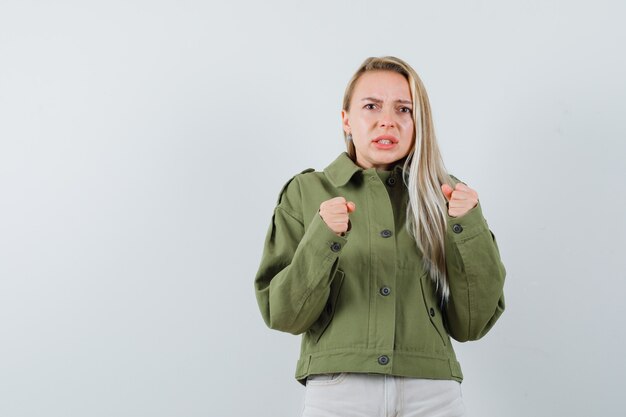 Blonde lady standing in fight pose in jacket, pants and looking angry. front view.