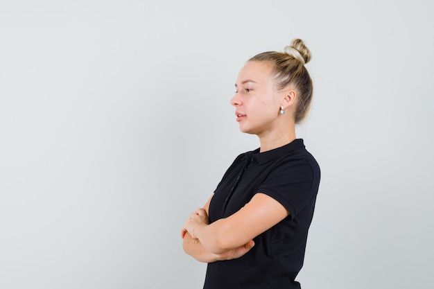 Blonde lady standing with crossed arms in black t-shirt and looking confident .