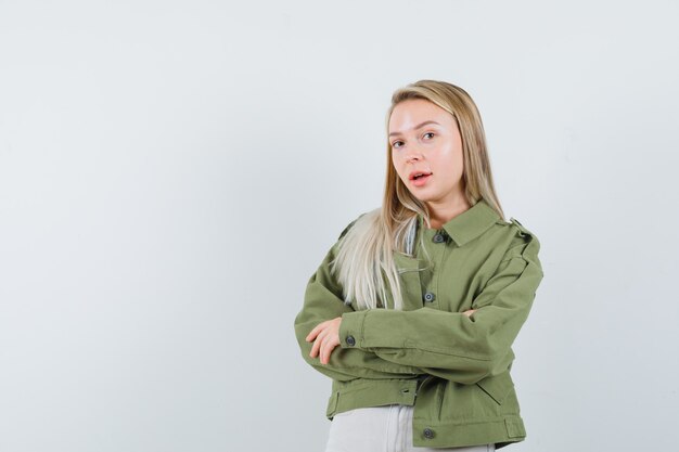 Blonde lady standing with crossed arms in jacket, pants and looking elegant , front view.