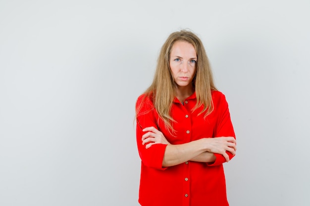 Blonde lady standing with crossed arms in red shirt and looking sad ,