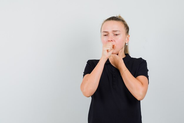 Blonde lady suffering from cough in black t-shirt and looking sick. front view.