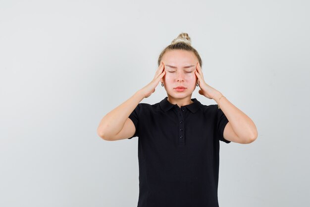 Blonde lady suffering from headache in black t-shirt and looking tired. front view.