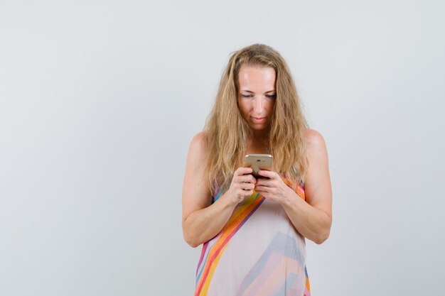 Blonde lady in summer dress typing on mobile phone and looking busy 