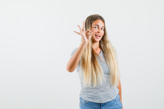 Blonde lady in t-shirt showing ok gesture and looking pleased , front view.