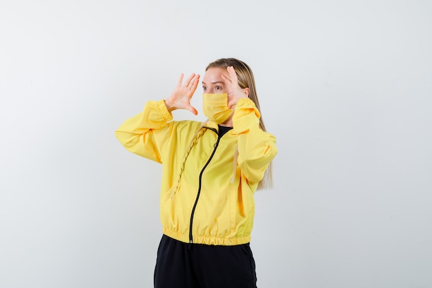 Free photo blonde lady in tracksuit, mask looking far away with hands near head and looking wondered , front view.
