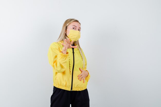 Blonde lady in tracksuit, mask showing stop gesture and looking focused , front view.