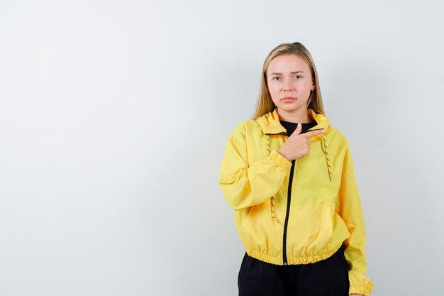 Blonde lady in tracksuit pointing right and looking sensible , front view.