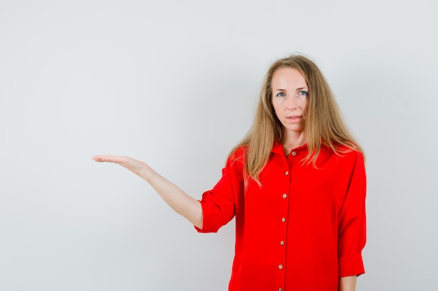 Blonde lady welcoming or showing something in red shirt and looking confident ,