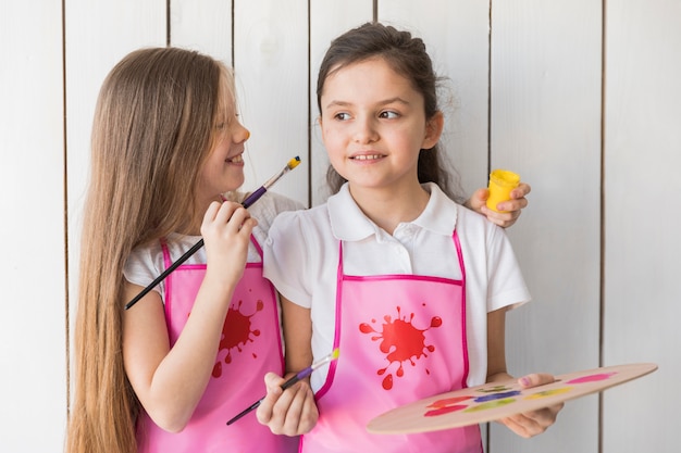 Blonde little girl painting on her friend's cheek with paint brush