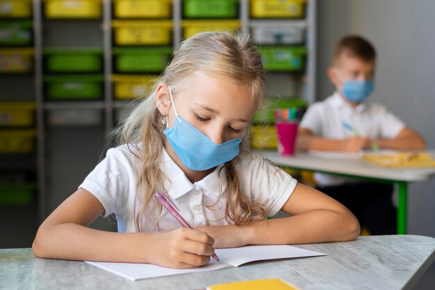 Blonde little girl writing while wearing a medical mask