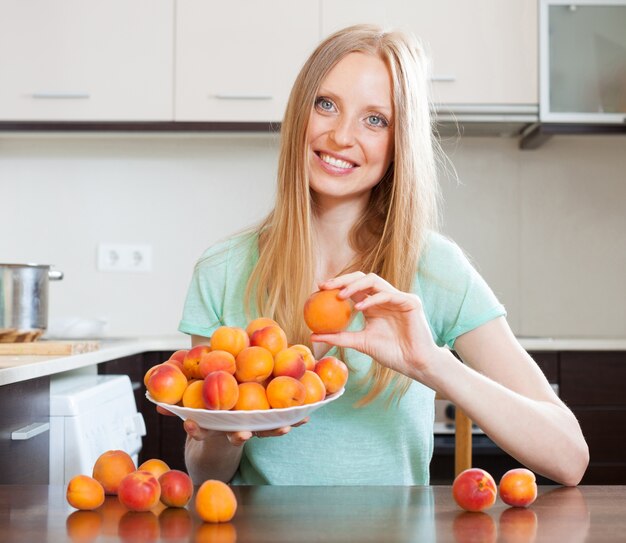 blonde long-haired girl holding apricots in home kitchen 