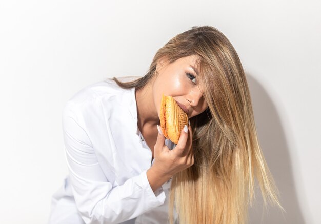 Белокурая модель в белой рубашке соблазнительно ест бутерброд.