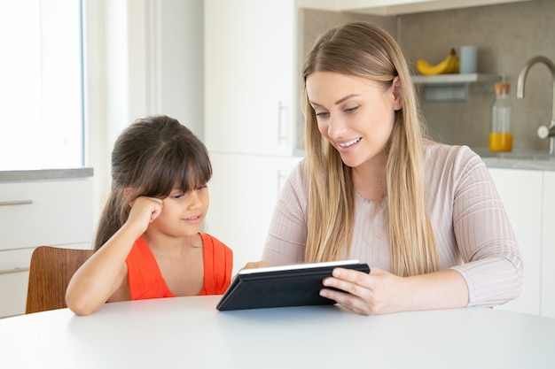 Blonde mom holding tablet and showing it to daughter.