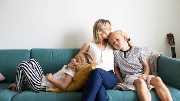 Блондинка мама целует голову сына и расслабляется с дочерью на диване