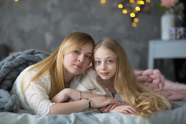 Blonde mom and teen daughter hug on bed