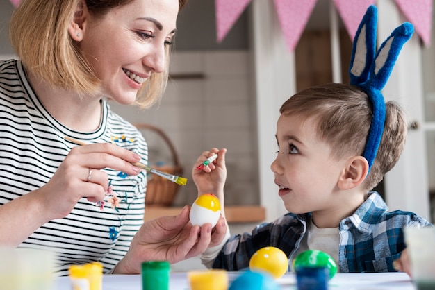 Blonde mother teaching her son how to paint eggs for easter