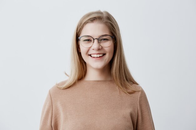 금발 농담 젊은 유럽 여성 좋은 농담을 웃고, 완벽한 하얀 치아, 그녀의 표정과 기쁨과 행복의 전체 표현을 보여주는 갈색 특대 스웨터를 입고. 사람과 생활