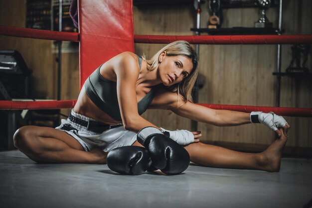 Blonde pretty woman is warming up before sparring while sitting at her corner on the ring.