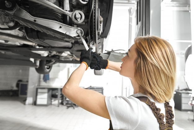 Free photo blonde repairing auto undercarriage with wrench.